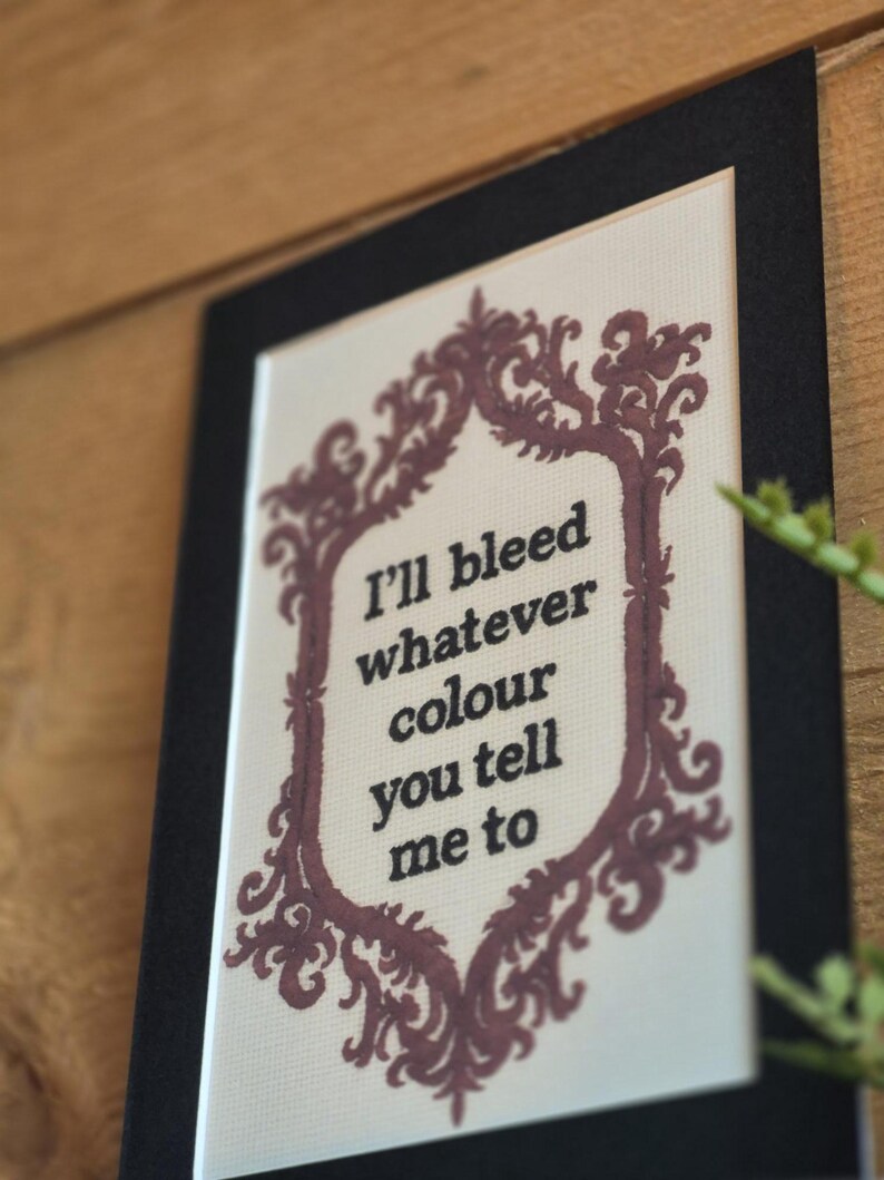 K&ouml;nnte beinhalten: Ein gerahmtes Kunstwerk mit dem Text "I'll bleed whatever colour you tell me to." Der Text ist schwarz, umgeben von einem burgunderfarbenen dekorativen Rahmen. Das Kunstwerk ist vor einem wei&szlig;en Hintergrund platziert und schwarz gerahmt.