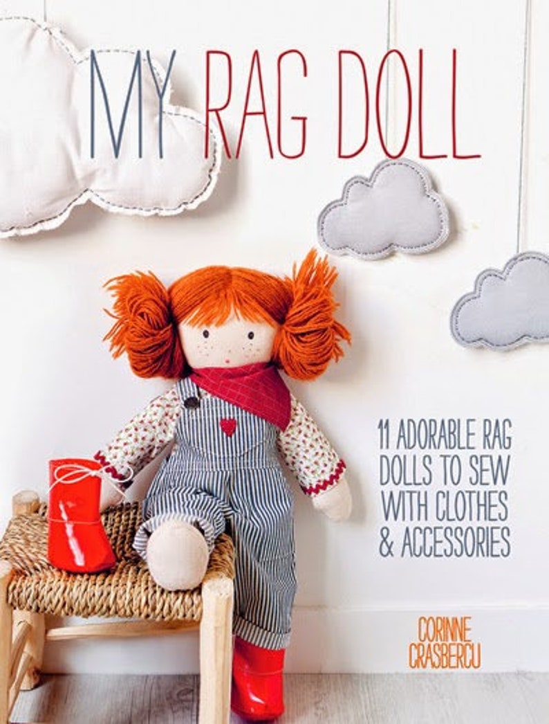 May include: A red-haired rag doll wearing a blue and white striped overall dress and a red bandana. The doll is sitting on a wicker stool with red shoes. The book cover reads "My Rag Doll" and "11 Adorable Rag Dolls to Sew with Clothes & Accessories".