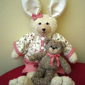 May include: A white plush bunny wearing a red and white gingham dress with a floral print and a red bow. The bunny is holding a brown plush teddy bear wearing a red bow.
