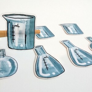 May include: A set of seven blue glass laboratory beakers and flasks with markings for measuring liquids. The beakers and flasks are arranged on a white surface.