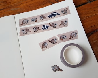 May include: A sheet of washi tape with a repeating pattern of raccoons and a single skunk. The tape is on a white surface with a roll of tape and a single raccoon sticker.
