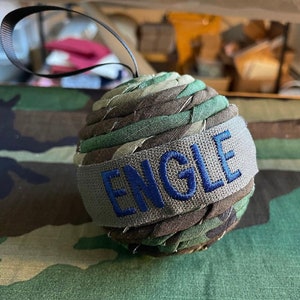 May include: A green, brown, and gray fabric ornament with the name "ENGLE" embroidered in blue on a gray band.