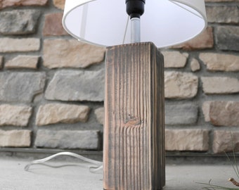 May include: A rustic wooden lamp base with a white lampshade. The base is made of reclaimed wood and has a natural, weathered finish.