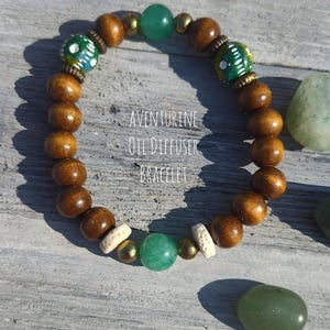 May include: Aventurine oil diffuser bracelet. The bracelet features large, round, wooden beads, interspersed with green aventurine beads, gold-colored beads, and decorative beads with a green and white pattern. The text "AVENTURINE OIL DIFFUSER BRACELET" is visible.