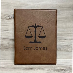 May include: A brown leather journal with a black scales of justice design and the name "Sam James" embossed on the front.