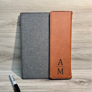 May include: A brown leather and gray fabric folder with the initials "A/M" engraved on the front.
