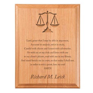 May include: A wooden plaque with a carved image of a scale of justice and a poem about the legal profession. The plaque is inscribed with the text "Lord, grant that I may be able in argument, Accurate in analysis, strict in study, Candid with clients and honest with adversaries. Sit with me at my desk and listen with me to my client's plaints, read with me in my library, And stand beside me in court, so that today I shall not, in order to win a point, lose my soul AMEN Richard M. Leick".