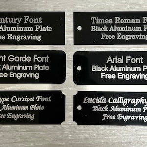 May include: Six black rectangular aluminum plates with different fonts engraved on them. Each plate has the text "Black Aluminum Plate" and "Free Engraving" on it. The fonts are Century, Times Roman, Avant Garde, Arial, Monotype Corsiva, and Lucida Calligraphy.
