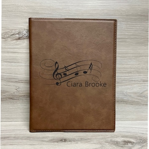May include: A brown leather music notebook with a musical note design and the name "Ciara Brooke" engraved on the front.
