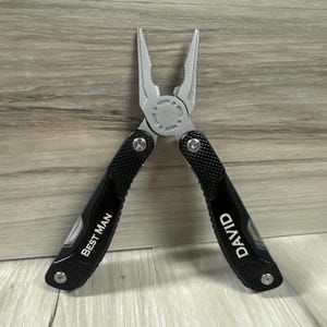 May include: Black multi-tool pliers with a textured black handle. The handle is engraved with the words "Best Man" and "David".