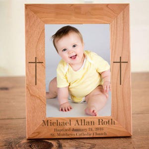 May include: A wooden picture frame with a cross engraved on each side. The frame holds a photo of a baby boy with the text "Michael Allan Roth Baptized January 24, 2016 St. Matthews Catholic Church".