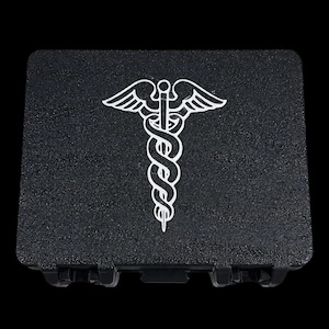 May include: A rectangular black storage case with a textured surface featuring a white caduceus symbol printed on the center of the lid. The case has a hinged design with visible locking latches along the bottom edge against a black background.