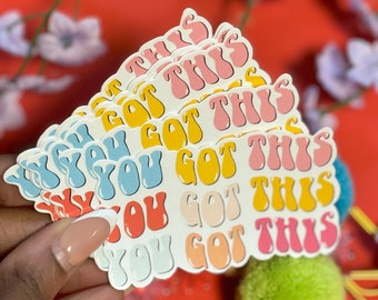 May include: A stack of colorful stickers with the phrase "You Got This" in a retro font. The stickers are in shades of pink, blue, yellow, and orange.