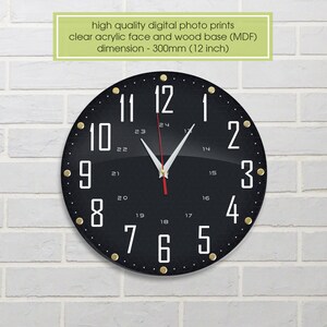 May include: A black clock with white numbers and gold accents. The clock face is 12 inches in diameter and has a clear acrylic face and a wood base.