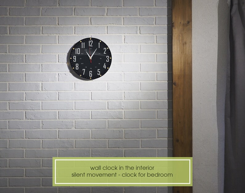 May include: A black wall clock with white numbers and gold accents hangs on a white brick wall. The clock has a silent movement and is ideal for a bedroom.