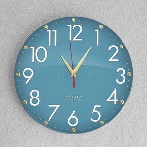 Op de afbeelding: Een blauwe ronde wandklok met witte cijfers en gouden accenten. De klok heeft een quartz-uurwerk en is stil.
