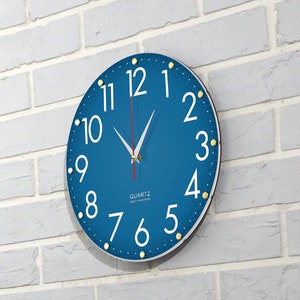 May include: A blue round clock with white numbers and gold accents. The clock face has a textured pattern and the words "QUARTZ" and "JAPAN MOVEMENT" are printed on the face.