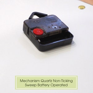 May include: Close-up of a black quartz clock mechanism with a red button. The text "QUARTZ" is visible on the mechanism. Mechanism Quartz Non-Ticking Sweep Battery Operated.