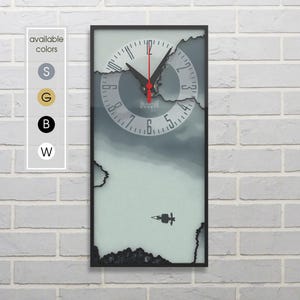 Peut inclure: Une horloge avec un design de visage fissuré. Le cadran de l'horloge est blanc avec des chiffres et des aiguilles noirs. L'horloge est encadrée de noir et a un fond gris.