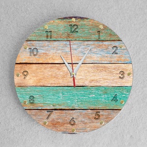 Könnte beinhalten: Eine runde Uhr mit Holzmaserung in Braun-, Beige- und Blautönen. Das Zifferblatt hat schwarze römische Ziffern als Stundenmarkierungen und goldene Akzente.