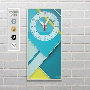 Könnte beinhalten: Eine türkisfarbene, gelbe und weiße geometrische Uhr mit schwarzen Zahlen und Zeigern. Die Uhr ist weiß gerahmt und hat einen weißen Hintergrund.