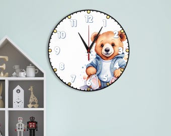May include: A round wall clock with a white face featuring a brown bear illustration wearing a blue jacket. The clock has black hour and minute hands, a thin red second hand, and large light blue numbers from 1 to 12 around the perimeter.