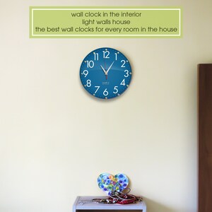 May include: A blue wall clock with white numbers and hands against a light yellow wall. The clock is round and has a silver frame. The text "wall clock in the interior light walls house the best wall clocks for every room in the house" is above the clock.