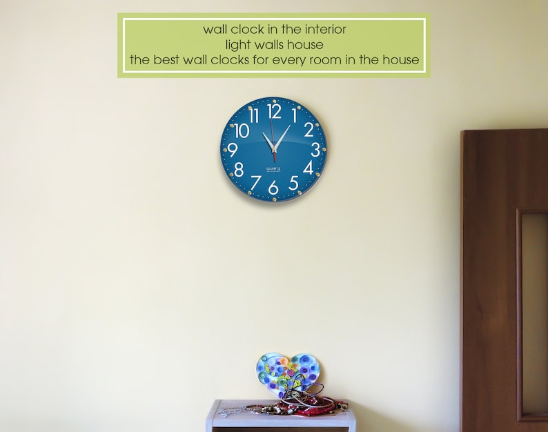 May include: A blue wall clock with white numbers and hands against a light yellow wall. The clock is round and has a silver frame. The text "wall clock in the interior light walls house the best wall clocks for every room in the house" is above the clock.