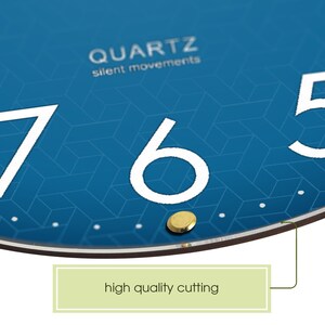 May include: Close-up of a blue clock face with white numbers 7, 6, and 5. The clock face has a geometric pattern and the text "QUARTZ silent movements" is printed at the top. The clock face is surrounded by a brown frame.