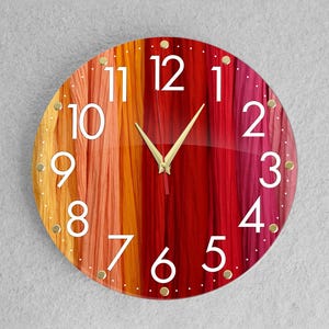 Puede incluir: Un reloj redondo con un fondo a rayas rojo, naranja y amarillo. La esfera del reloj tiene números blancos y manecillas doradas.