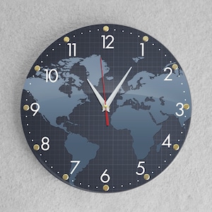Puede incluir: Un reloj redondo de color azul oscuro con detalles dorados y números blancos. La esfera del reloj presenta un diseño de mapa del mundo con una aguja de hora roja y una aguja de minutos blanca.