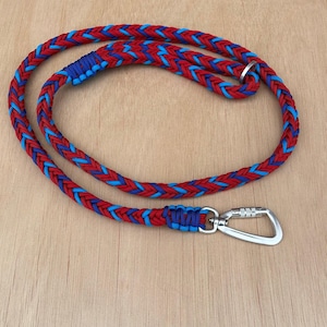 Puede incluir: Una correa de cuerda trenzada roja y azul con un mosquetón plateado. La correa está hecha de una cuerda gruesa y duradera con un patrón de hebras rojas y azules entrelazadas. La correa está diseñada para uso con mascotas.