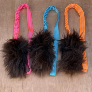 Peut inclure: Trois jouets pour chiens avec des boules duveteuses marron foncé et des poignées colorées. Les poignées sont roses, bleues et orange, avec un cordon élastique assorti. Conçus pour le jeu interactif et le lancer.