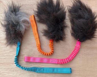 May include: Three cat toys with fluffy, dark gray and black feather ends. Each toy has a different colored handle: blue, orange, and pink. The handles are made of elastic and fabric.