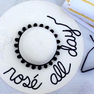 May include: White sun hat with black pom pom trim and black embroidery that reads "ros&eacute; all day".