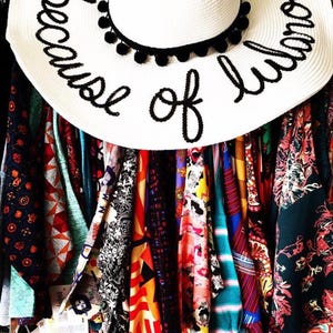 May include: A white sun hat with black pom pom trim and the text "because of love" written in black embroidery.