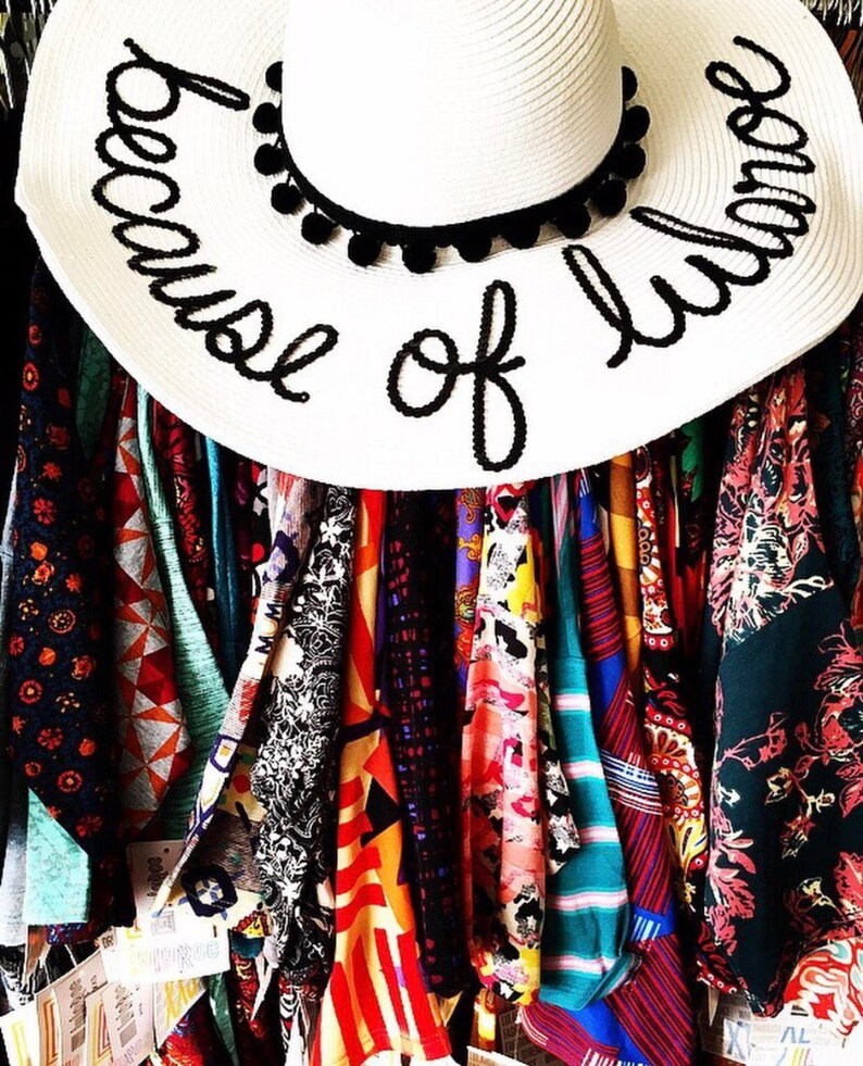 May include: A white sun hat with black pom pom trim and the text "because of love" written in black embroidery.