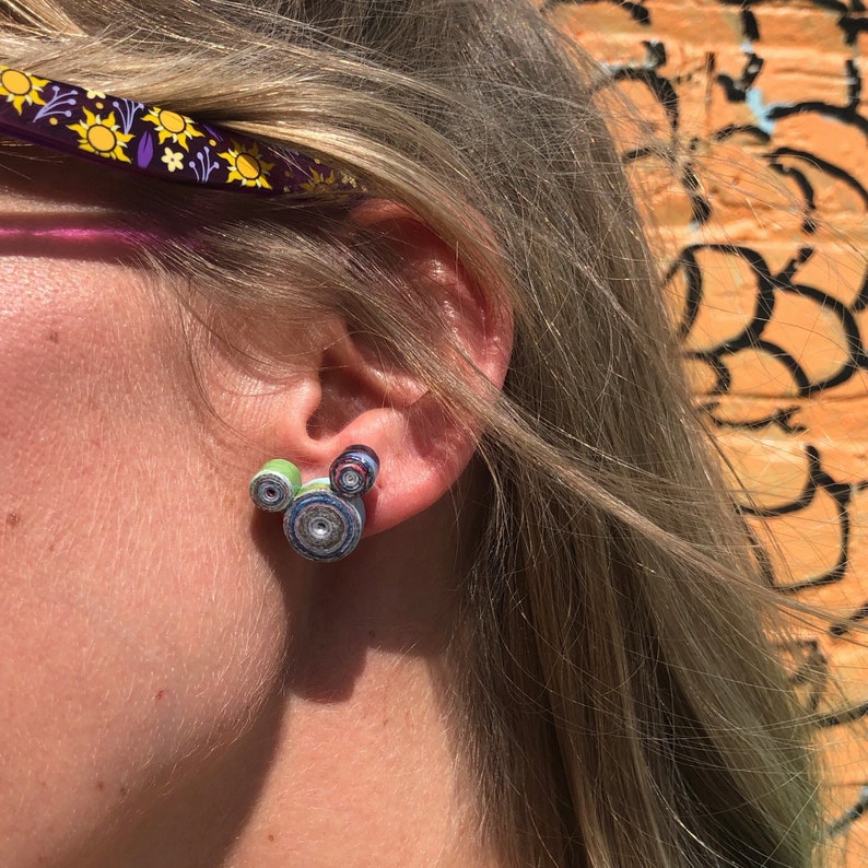 May include: A pair of colorful, paper-rolled earrings shaped like Mickey Mouse's head. The earrings are green, blue, and white.
