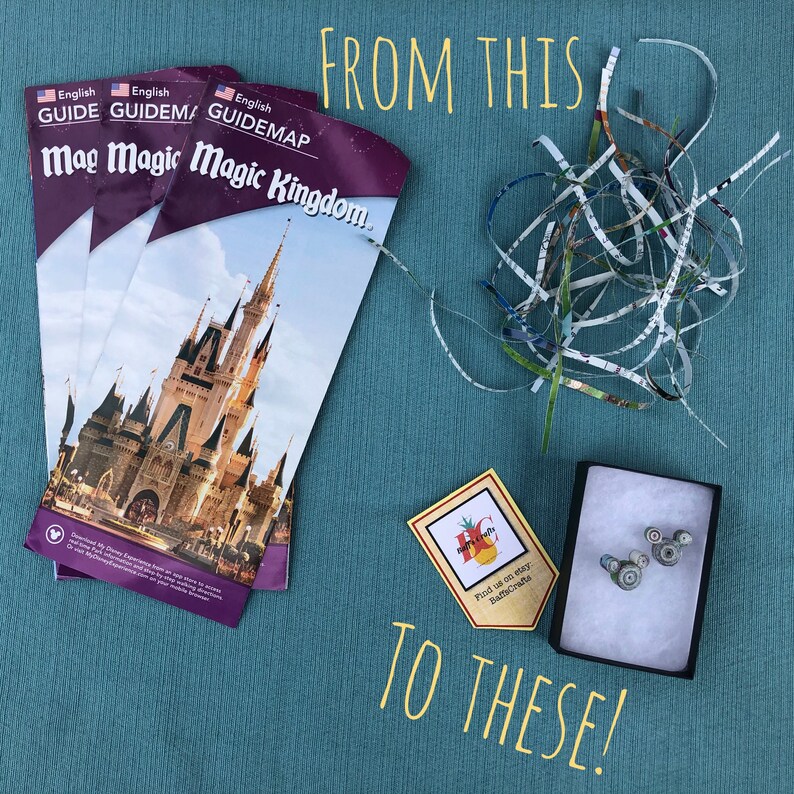 May include: A close-up of a small box with a pair of Mickey Mouse ears made from shredded paper. The box is sitting on a blue surface with a yellow sign that says "Find us on Etsy BaffeCrafte". There are three stacks of folded paper maps with the text "English Guidemap Magic Kingdom" on the front.