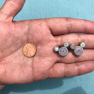 May include: A hand holding a US penny and five small, colorful, paper-rolled circles that resemble the Mickey Mouse head silhouette.