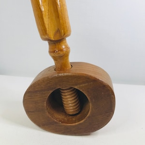 May include: A wooden nutcracker with a brown oval base and a brown wooden handle. The nutcracker has a threaded screw in the center.