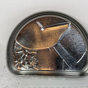 May include: A silver metal half-circle cake pan with a floral design and a small handle.