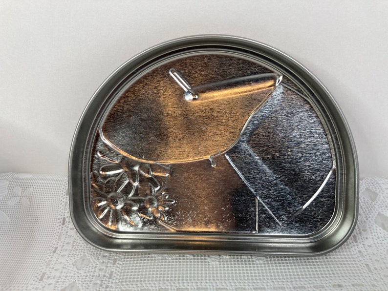 May include: A silver metal half-circle cake pan with a floral design and a small handle.