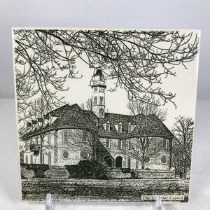 May include: A square, off-white tile featuring a black and white illustration of a building with a tall clock tower, trees, and the text "The Colonial Capitol". The tile is displayed on a clear acrylic stand.