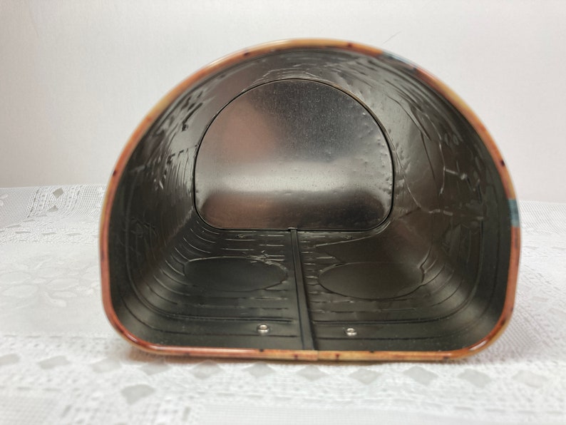 May include: The inside of a metal tin with a silver interior. The tin has a rounded shape and a decorative pattern on the outside.