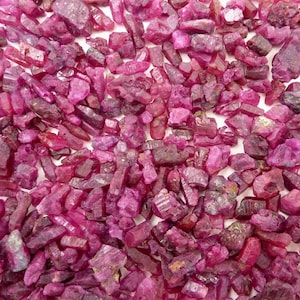 Może przedstawiać: Kolekcja surowych, nieoszlifowanych kamieni szlachetnych rubinu. Kamienie różnią się rozmiarem i kształtem, prezentując głęboki, czerwono-różowy odcień. Widoczna jest szorstka faktura i naturalne formacje kryształów.