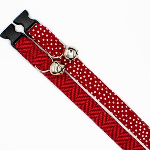 May include: Two red cat collars with bells. One collar has a white polka dot pattern and the other has a red and white chevron pattern.
