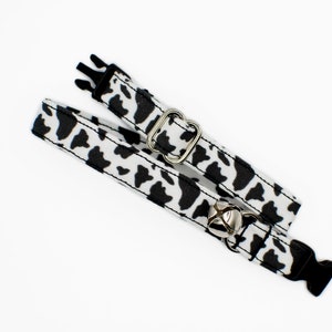 Peut inclure: Un collier de chat imprim&eacute; vache noir et blanc avec une clochette argent&eacute;e et une boucle en plastique noire.