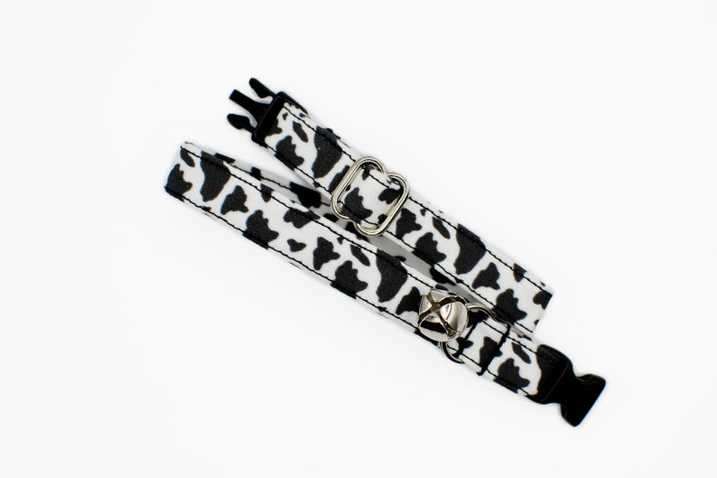 Peut inclure: Un collier de chat imprim&eacute; vache noir et blanc avec une clochette argent&eacute;e et une boucle en plastique noire.