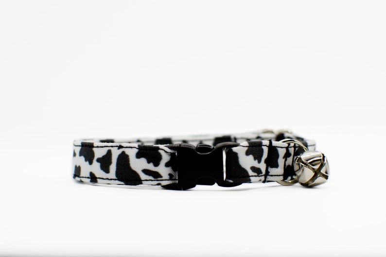 Peut inclure: Un collier de chat imprim&eacute; vache noir et blanc avec une boucle noire et une clochette argent&eacute;e.